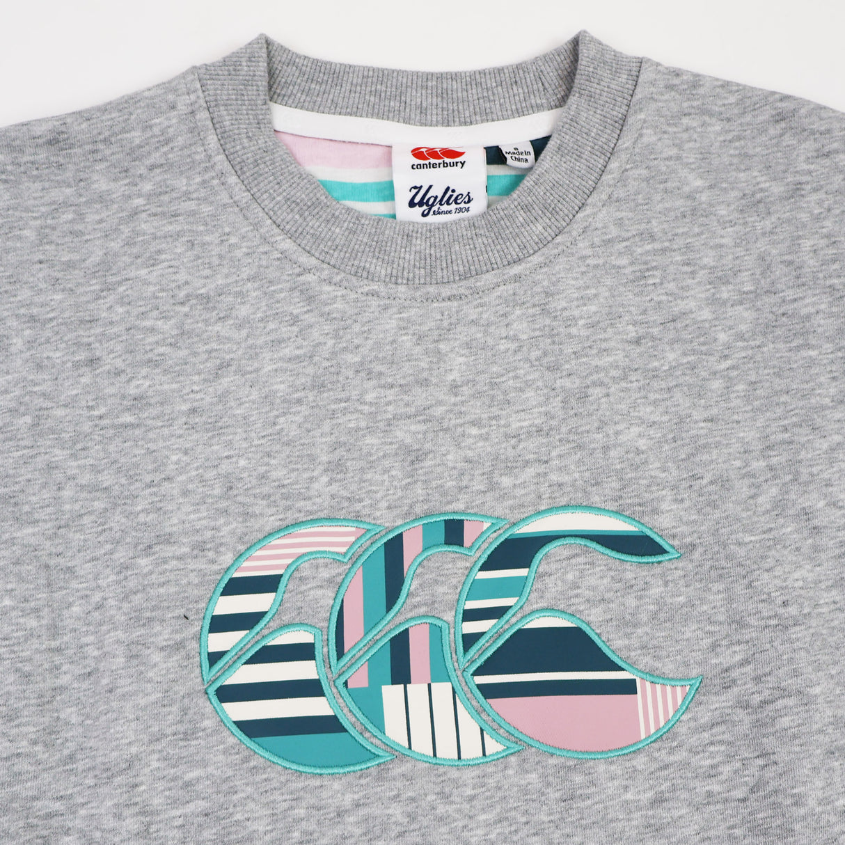 Close-up of the Canterbury Women's Uglies Logo Crew Sweatshirt in grey, showcasing a large, vibrant striped and patterned CCC logo design on the front—a perfect women's rugby sweatshirt from Canterbury.