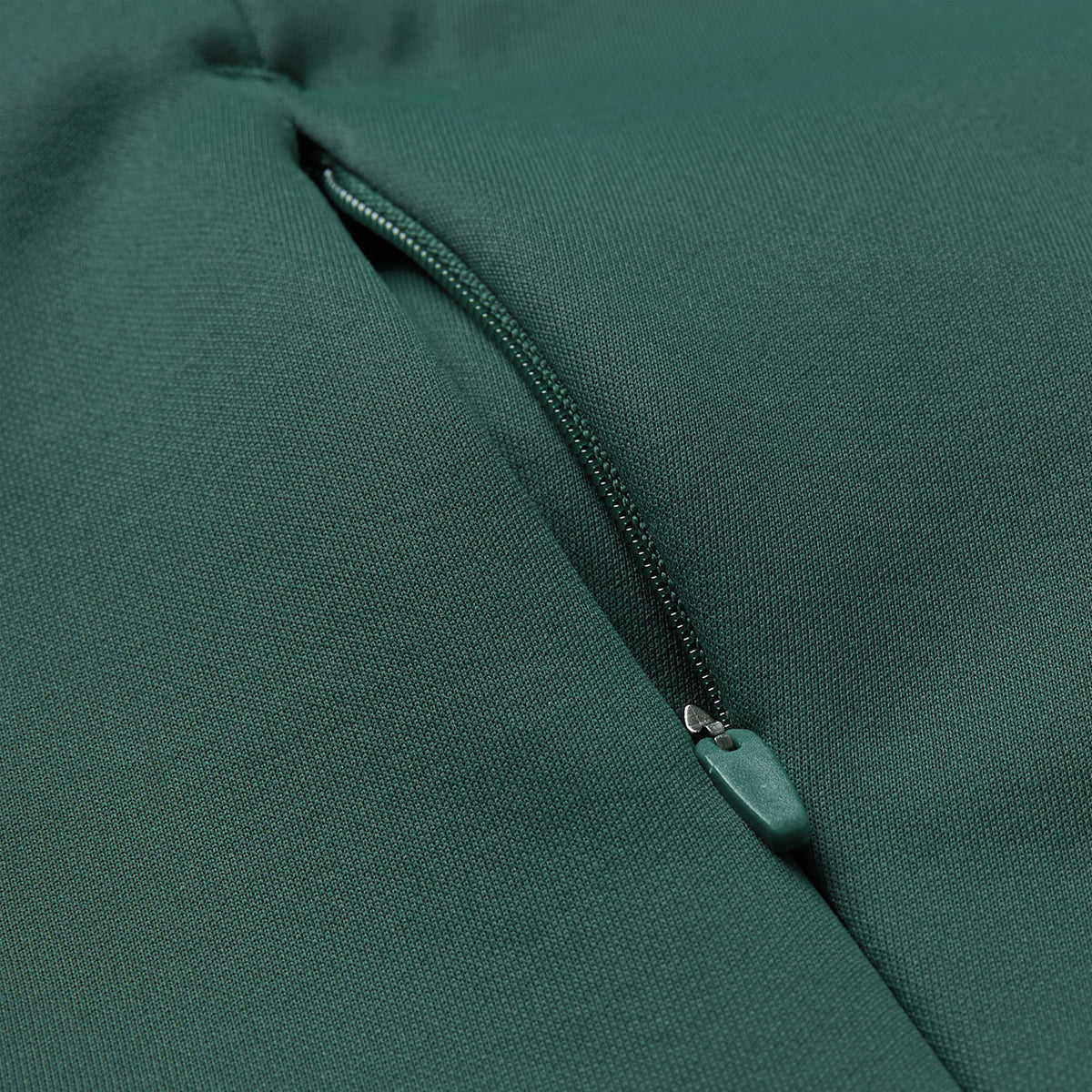 Close-up of the green fabric from the Ireland 26 OH Zip Training Hoodie by Canterbury, featuring a partially opened zipper that reveals the zipper teeth and pull tab.