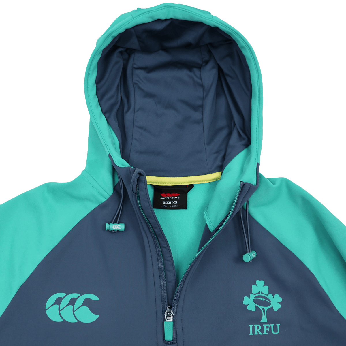 The Ireland 26/27 Summer Tour Training Hoodie by Canterbury features IRFU shamrock and CCC logos, a teal and navy design, flat lay with hood up and partial zip—ideal as a moisture-wicking training hoodie for the Ireland Summer Tour.