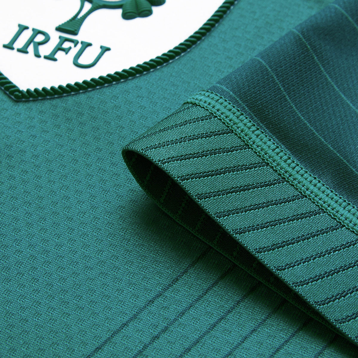 Close-up of a green jersey sleeve with thin stripes and the IRFU logo patch in the top left corner, highlighting the distinctive design of the Canterbury Ireland 26 Home Test Jersey.
