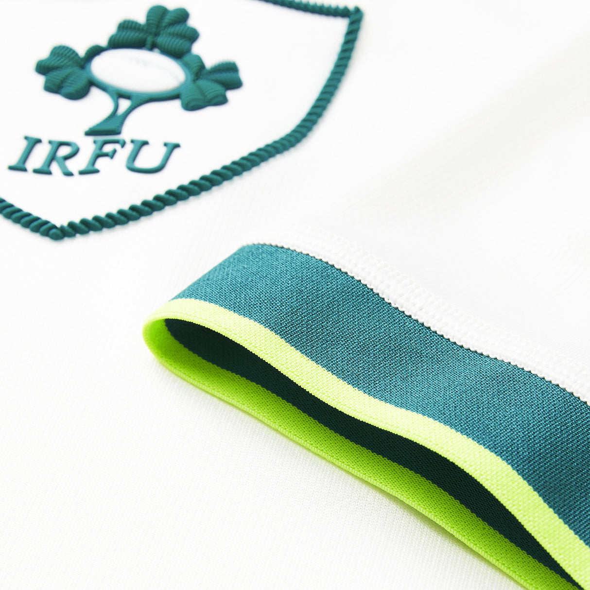 Close-up of the white fabric from the Ireland 26 Alternate Pro Jersey by Canterbury, featuring an IRFU logo patch and a sleeve with green, teal, and yellow stripes.