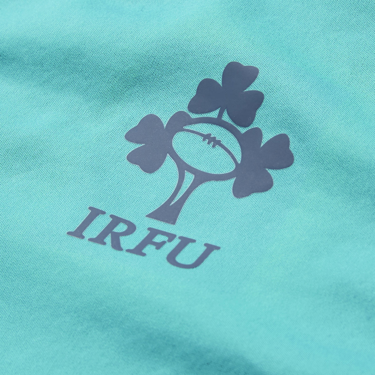 Close-up of the IRFU logo, showcasing a rugby ball and shamrock printed on teal fabric, from the Ireland 26 1/4 Zip Training Top by Canterbury, featuring advanced Thermoreg technology.