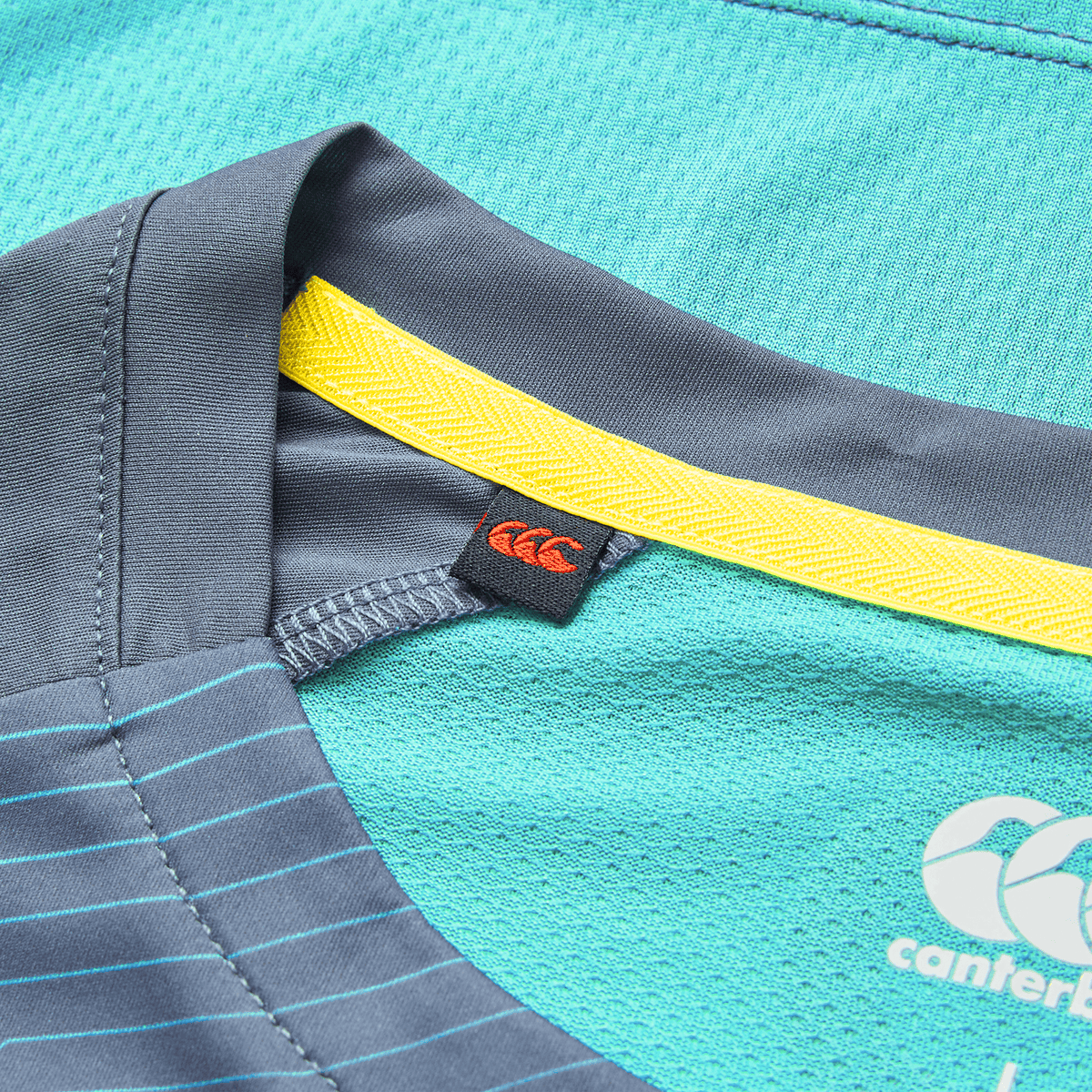 Close-up of the teal Ireland 26/27 Summer Tour Superlight Training Tee by Canterbury, featuring a gray collar, yellow trim, and red Canterbury logo tag.