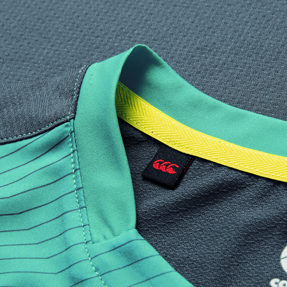 Close-up of the Ireland 26/27 Summer Tour Superlight Training Tank by Canterbury, featuring a teal collar with yellow inner trim, black tag with red logo, and detailed stitching—ideal for fans of lightweight training wear.