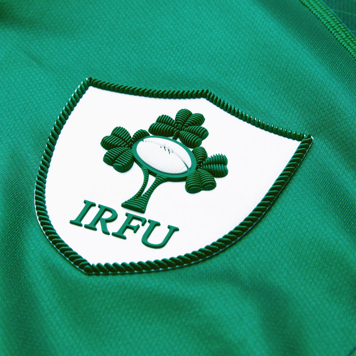 Close-up of the IRFU crest, featuring a rugby ball and shamrocks on green fabric, highlights the authentic detailing of the Youth Ireland 26 Home Pro Jersey by Canterbury.