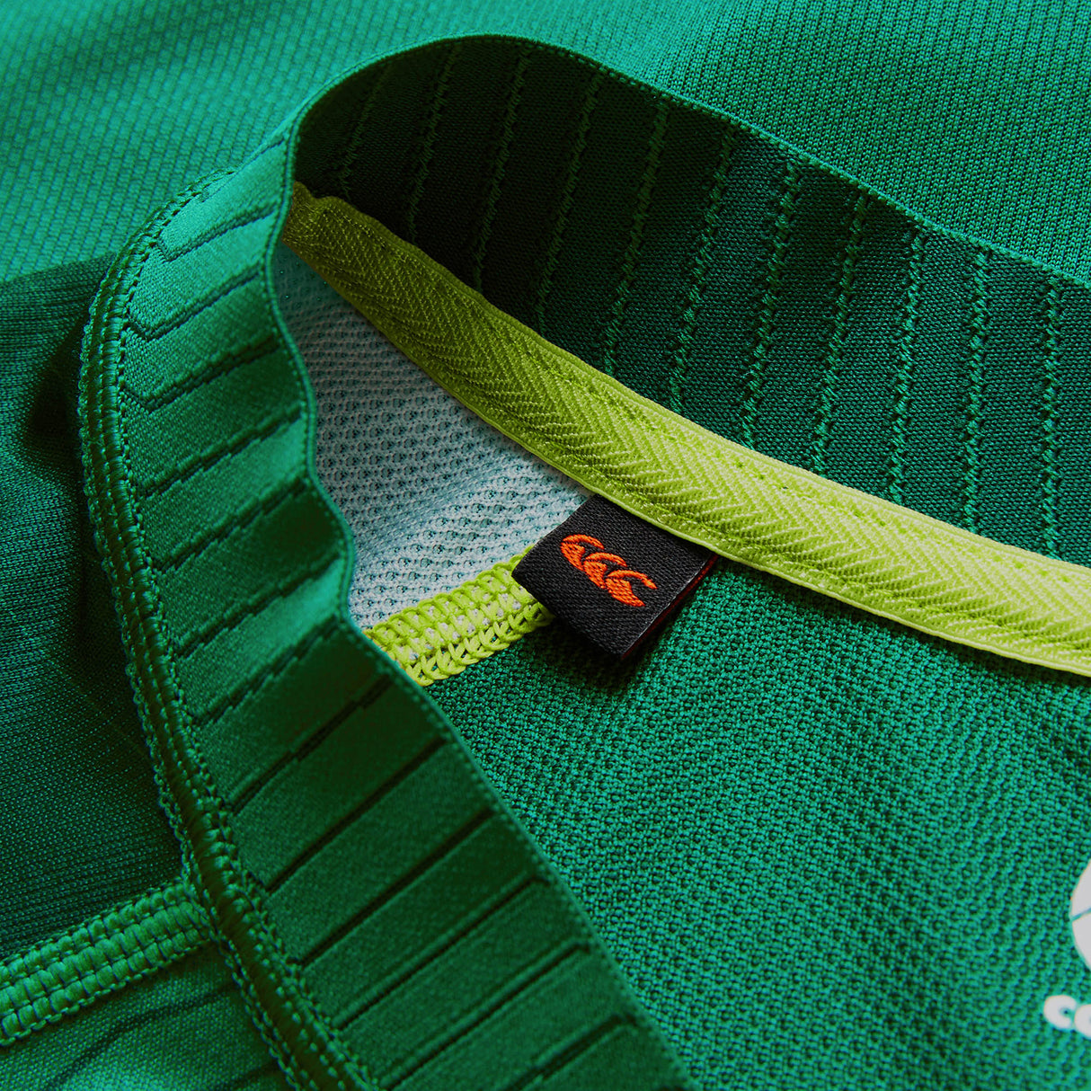 Close-up of the Youth Ireland 26 Home Pro Jersey by Canterbury, showcasing its textured green fabric, intricate stitching, yellow inner neckline band, and a black tag with Canterbury’s orange logo—all signature details that embody the authenticity of this Canterbury rugby jersey for youth.