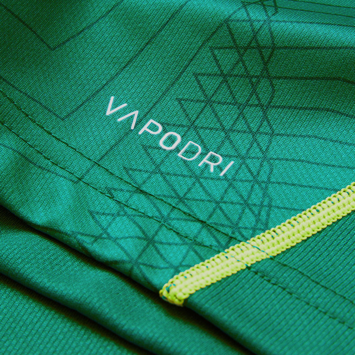 Close-up of green athletic fabric from the Youth Ireland 26 Home Pro Jersey by Canterbury, featuring the word “VAPODRI” printed in white and visible yellow stitching detail.