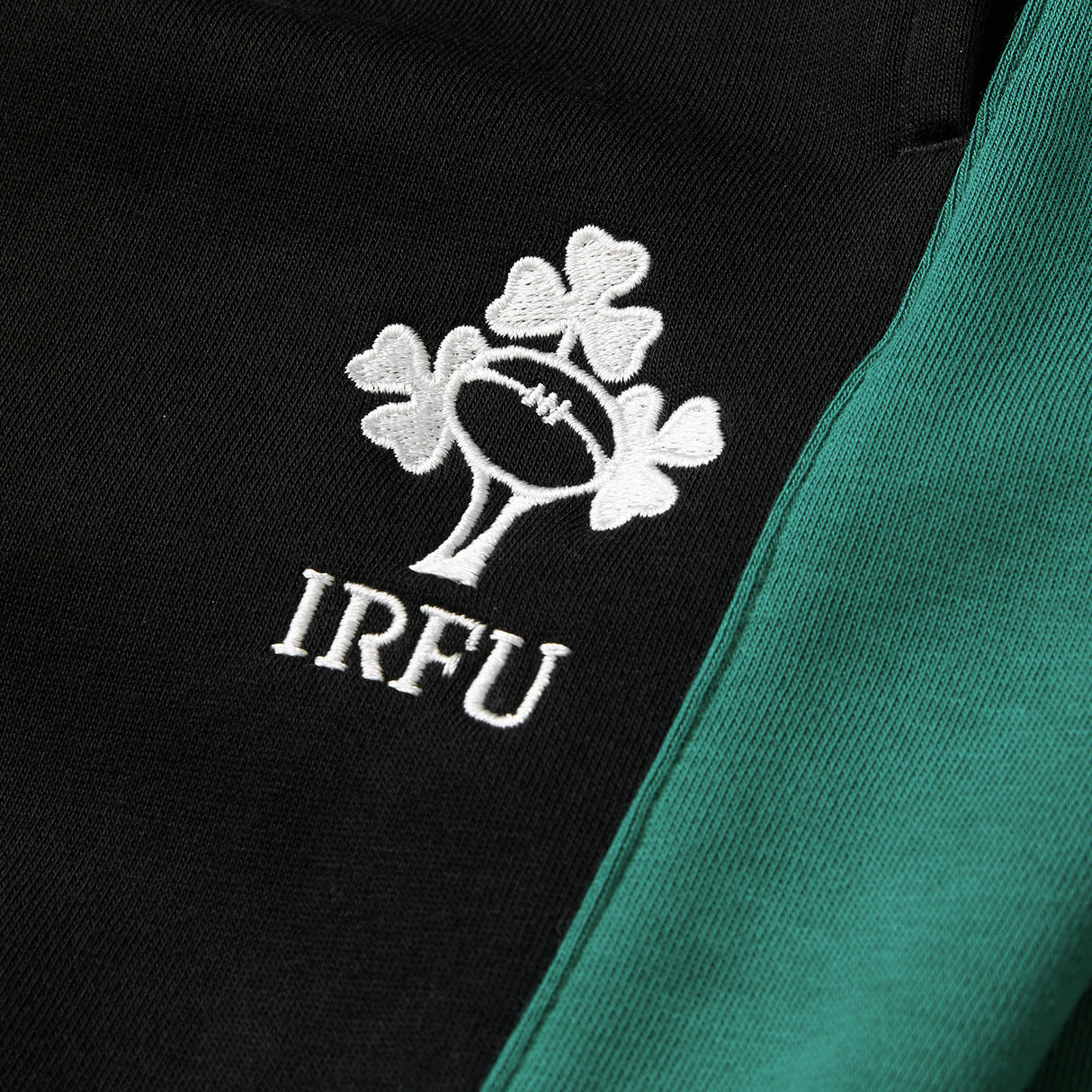 Close-up of a black and green fabric from the Canterbury Women’s Ireland 26 Legends Fleece Pant, featuring an embroidered white IRFU logo with three shamrocks and a rugby ball.