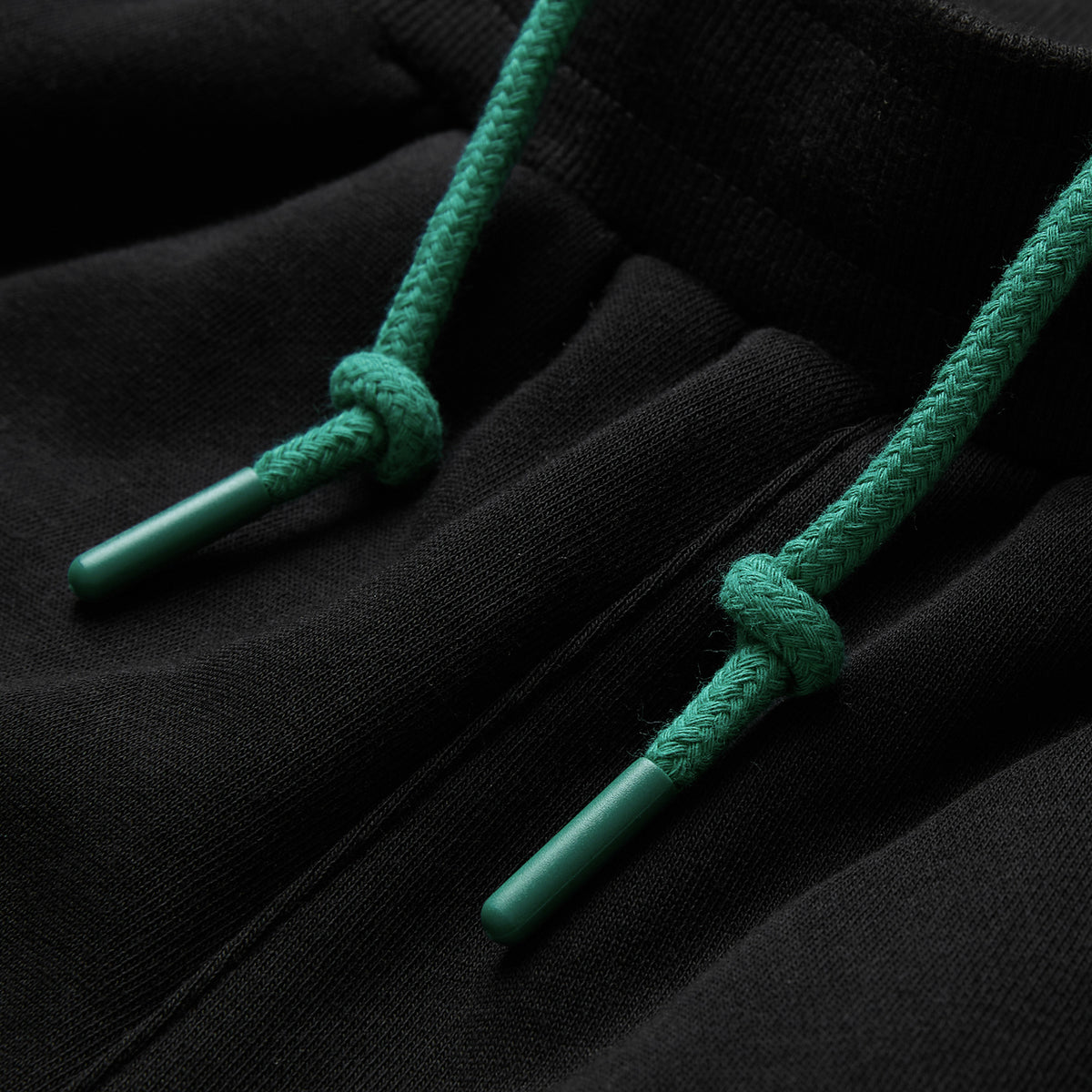 Close-up of a black hoodie with green drawstrings, highlighting the intricate knot detail and plastic aglets at each end, styled effortlessly with the Canterbury Women’s Ireland 26 Legends Fleece Pant for a sporty yet comfortable outfit.