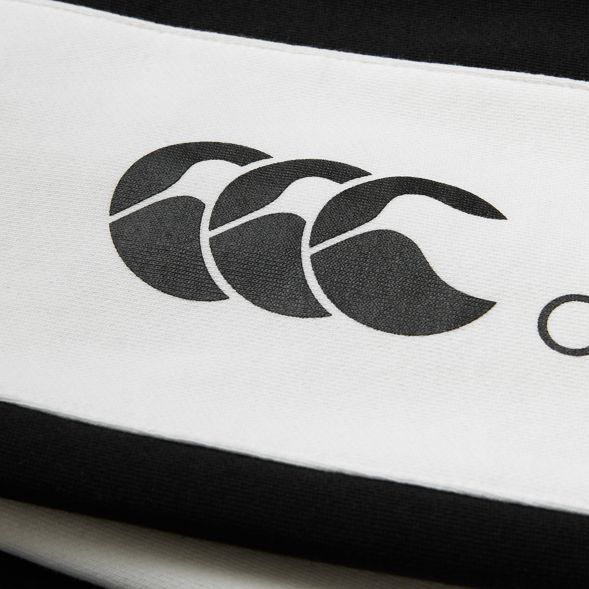 Close-up of a black and white striped fabric featuring the Canterbury logo with three overlapping stylized C’s, as seen on the Women’s Ireland 26 Legends Fleece Pant by Canterbury, echoing the iconic detailing found in classic Canterbury pant collections.