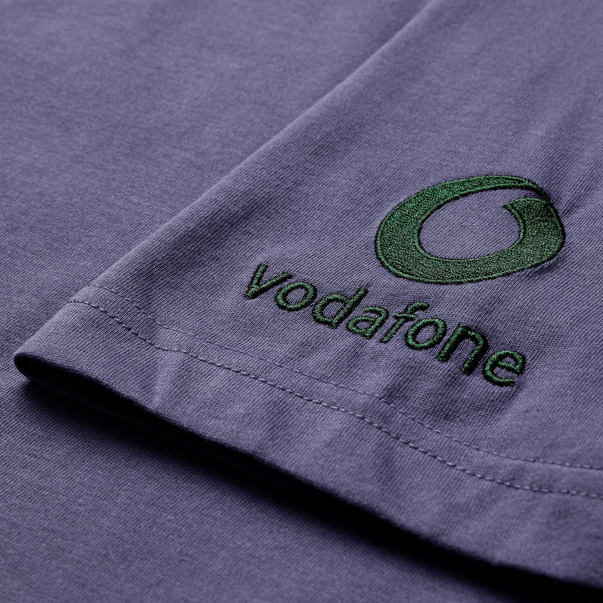 Close-up of a purple fabric featuring the brand logo and name embroidered in green thread near the edge, similar to the detailing on the Canterbury Women’s Ireland 26 Cotton T-shirt.