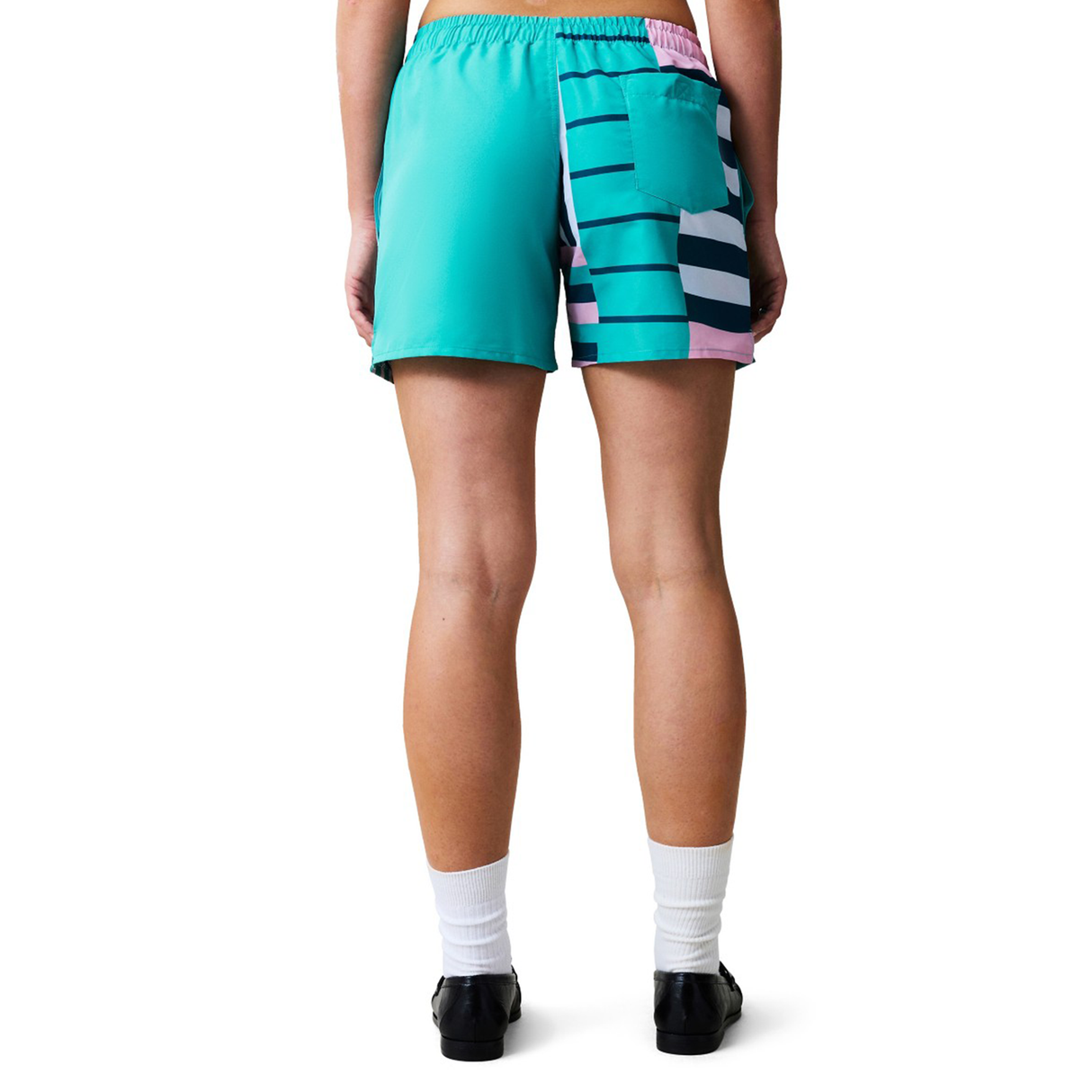 A person wears Women's Canterbury Uglies Harletic Short in teal with a striped back pocket, facing away; paired with white socks and black shoes. Ideal for those seeking durable athletic shorts from Canterbury.