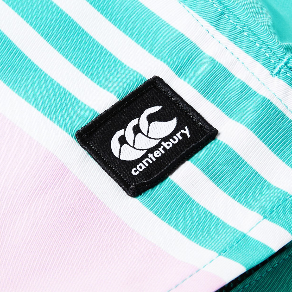 Close-up of the Women's Canterbury Uglies Harletic Short label, stitched on turquoise, white, and light pink fabric, highlighting the durability of these Canterbury athletic shorts.