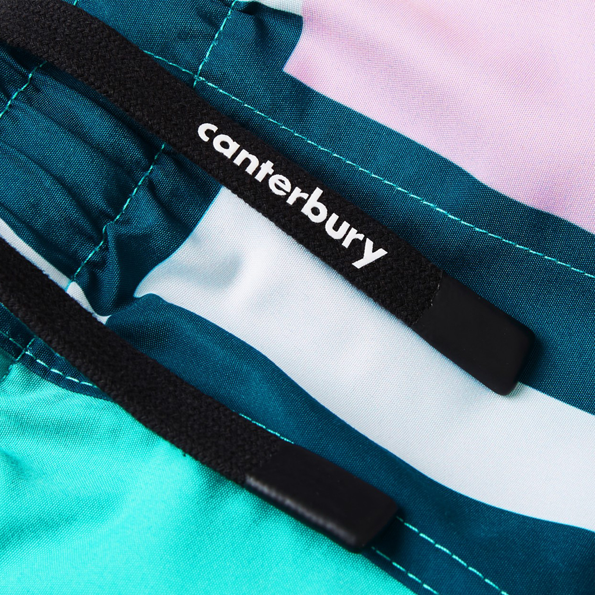 Close-up of two black drawstrings with "Canterbury" branding on the Women's Canterbury Uglies Harletic Short, featuring teal, turquoise, white, and pink color blocks for durable style in women's rugby.