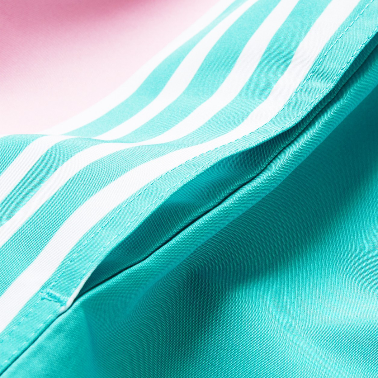 Close-up of Canterbury Women's Canterbury Uglies Harletic Short, featuring durable turquoise fabric with white diagonal stripes, displayed on a vibrant pink background.