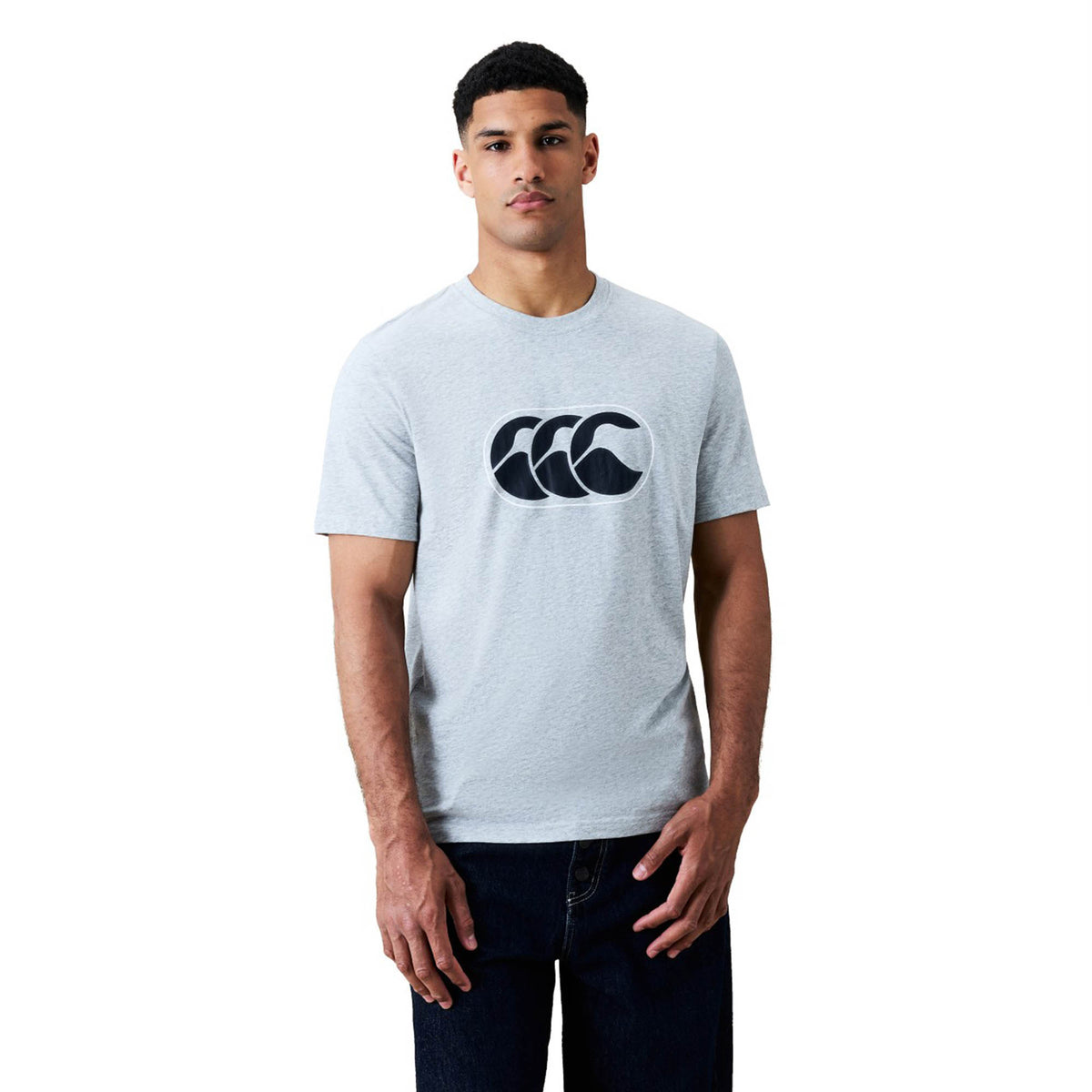 A man wearing a light gray Canterbury Rakaia 2.0 T-shirt featuring a bold black graphic logo on the chest stands against a plain white background, exemplifying classic Canterbury rugby apparel style.