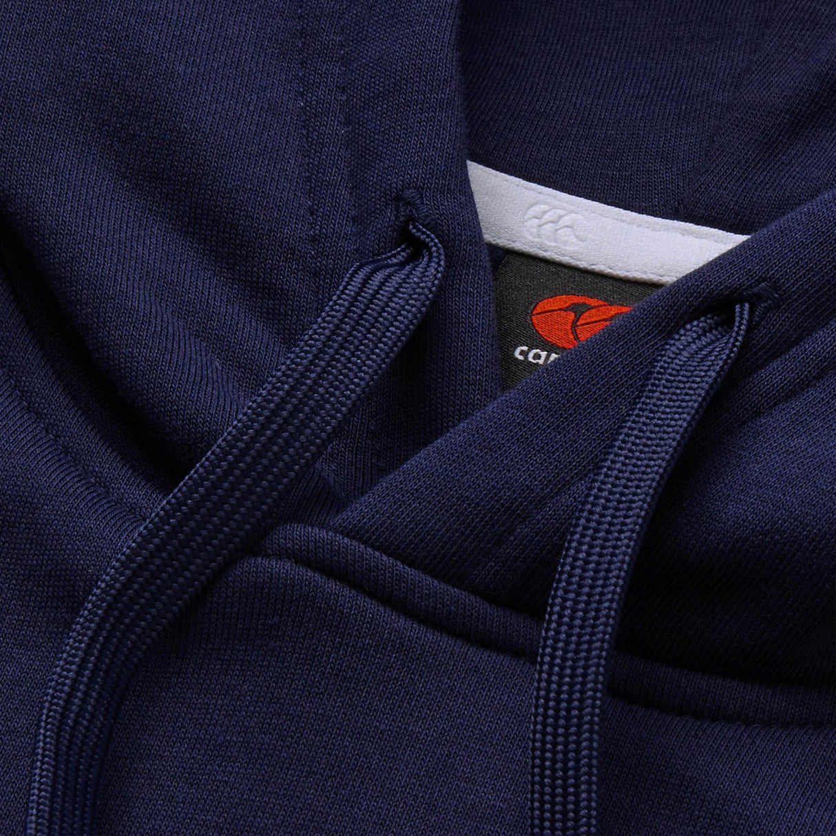Close-up of a navy blue Canterbury Rakaia 2.0 Hoodie featuring drawstrings and a visible black Canterbury tag with a red logo and partially visible white text.