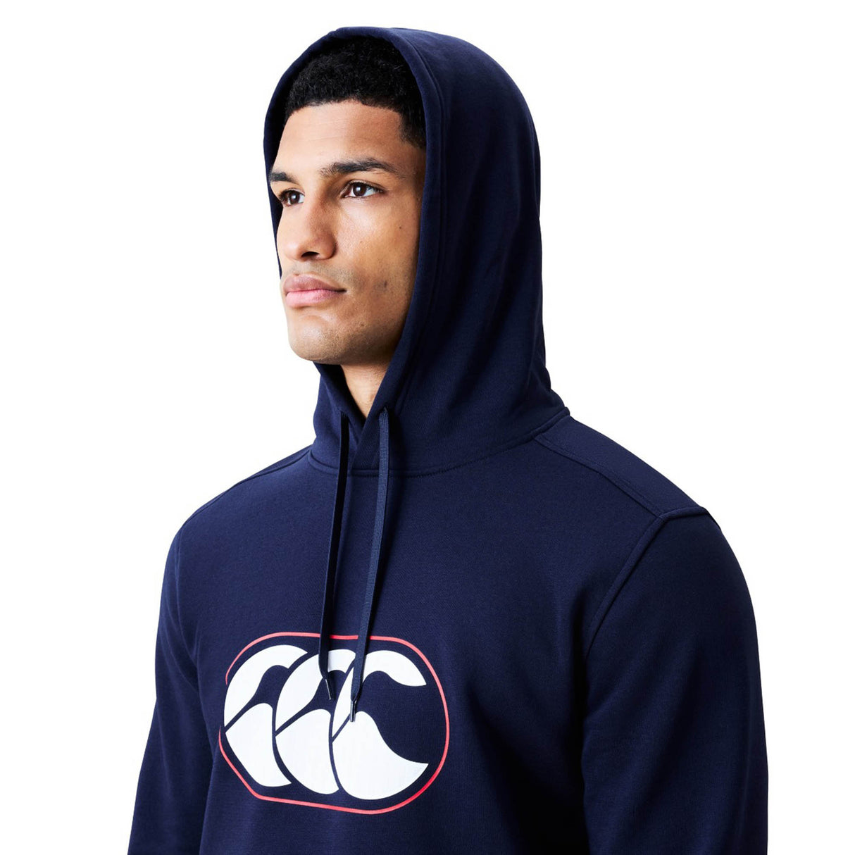 A man wears the Canterbury Rakaia 2.0 Hoodie in navy blue, featuring a white and red Canterbury logo on the chest, while looking off to the side against a plain white background.
