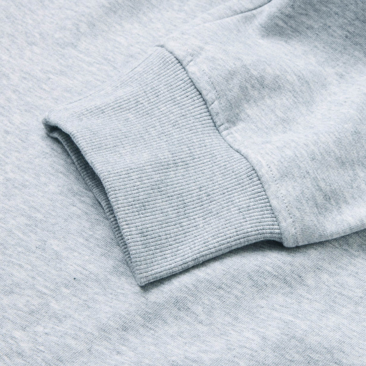 Close-up of a light gray sweatshirt sleeve with a ribbed cuff laid flat on a matching fabric background, showcasing the soft texture similar to that of Canterbury Rakaia 2.0 Fleece Pant by Canterbury.