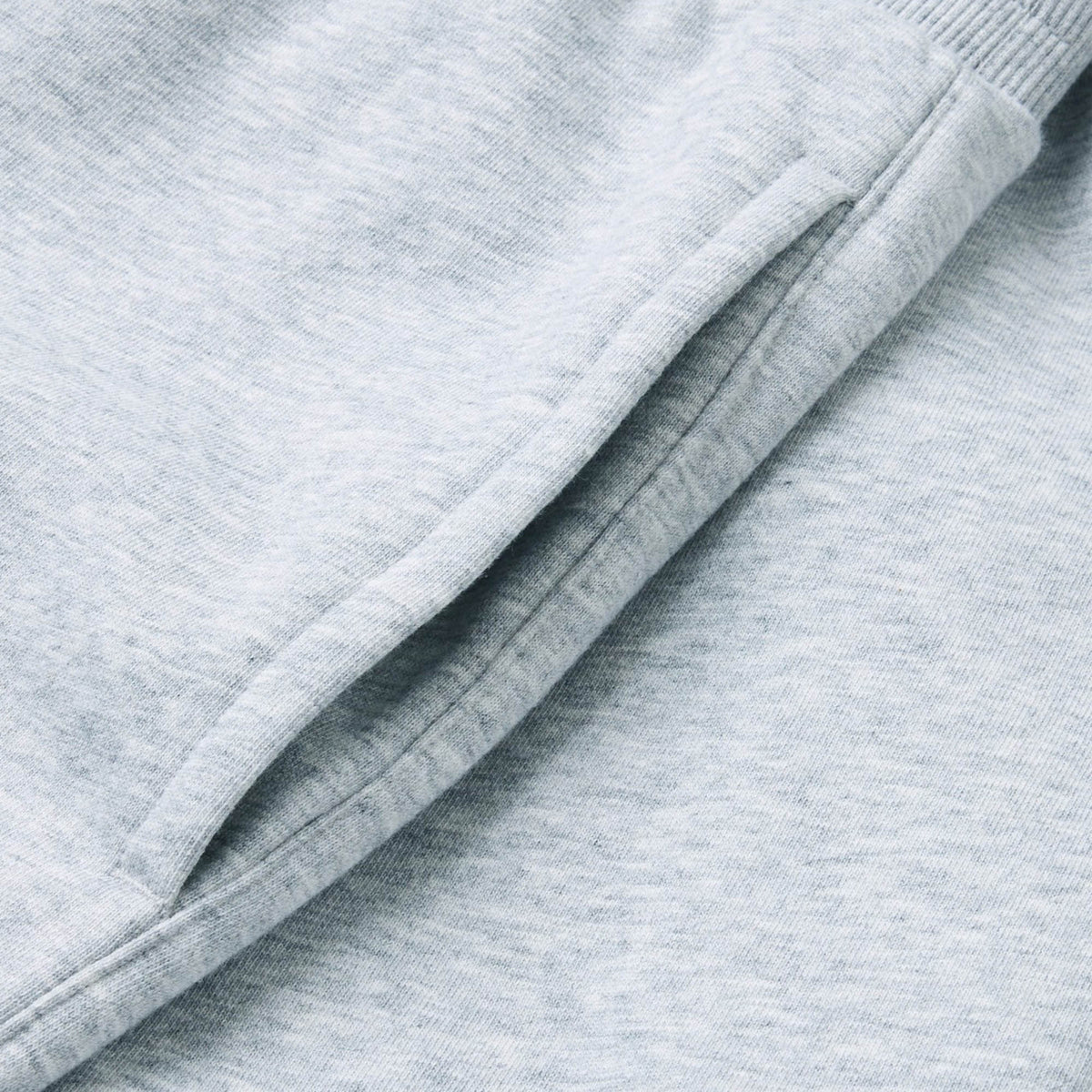 Close-up of the pocket on the Canterbury Rakaia 2.0 Fleece Pant in light grey, featuring visible stitching and a ribbed waistband, crafted from soft fleece fabric by Canterbury and set against a gentle fabric background.