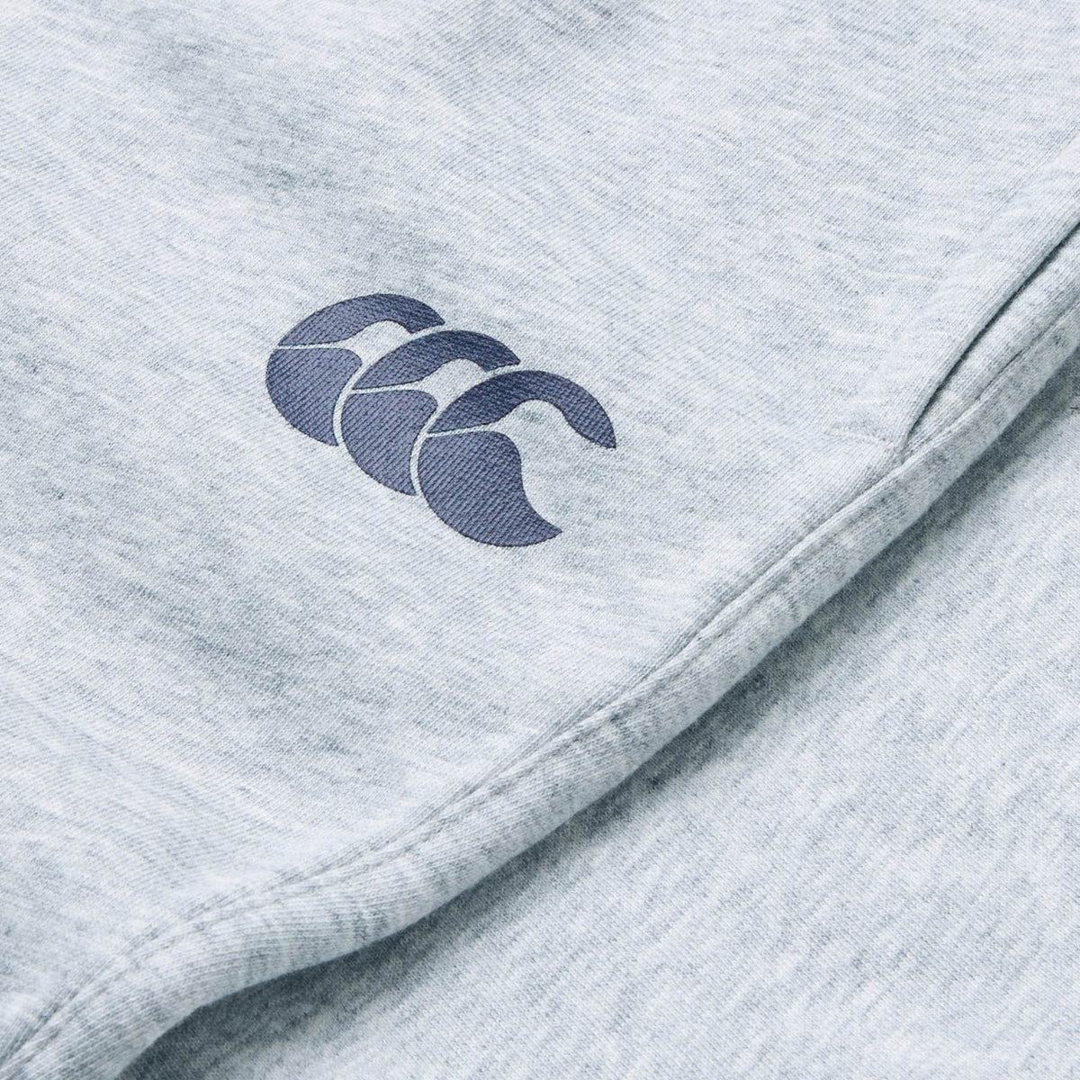 Close-up of the Canterbury Rakaia 2.0 Fleece Pant in light grey, featuring a dark blue stylized wave logo embroidered on it—ideal men’s track pants by Canterbury.