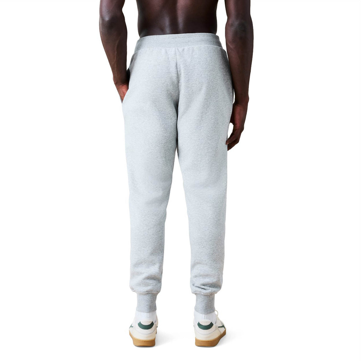 A person wearing Canterbury Rakaia 2.0 Fleece Pants in light gray and white sneakers is standing with their back to the camera against a white background.