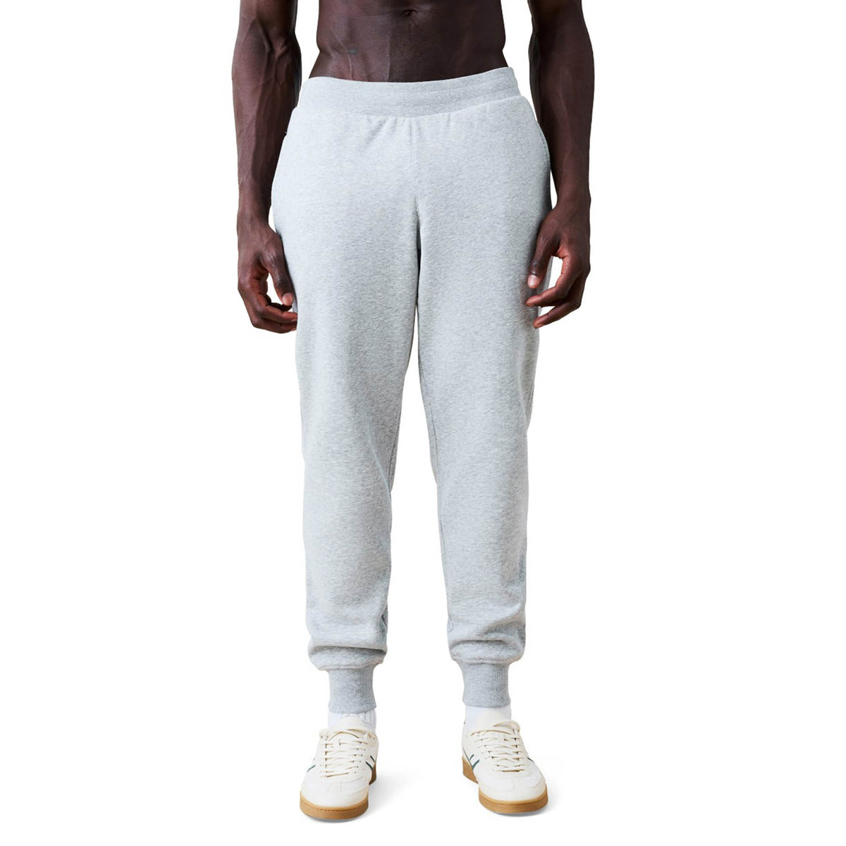 A person wearing Canterbury Rakaia 2.0 Fleece Pant jogger sweatpants in light gray and white sneakers is standing against a plain white background.