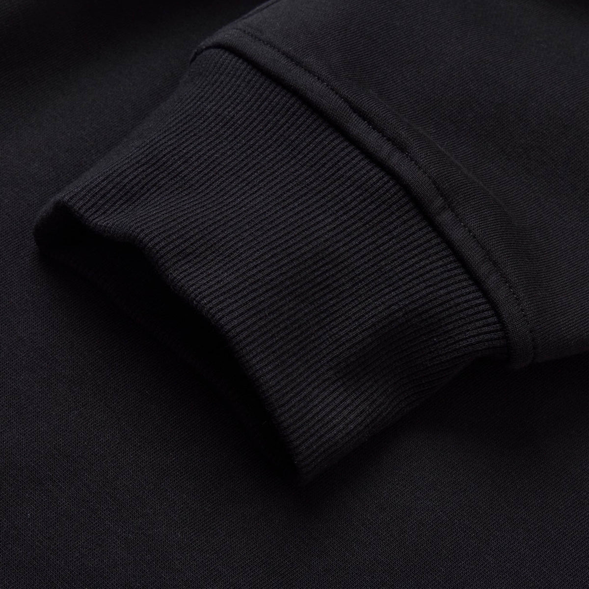 Close-up of a black sweatshirt sleeve cuff, featuring ribbed knit texture and precise stitching detail—perfect for pairing with men’s track pants or your favorite Canterbury Rakaia 2.0 Fleece Pant by Canterbury for a comfortable, coordinated look.