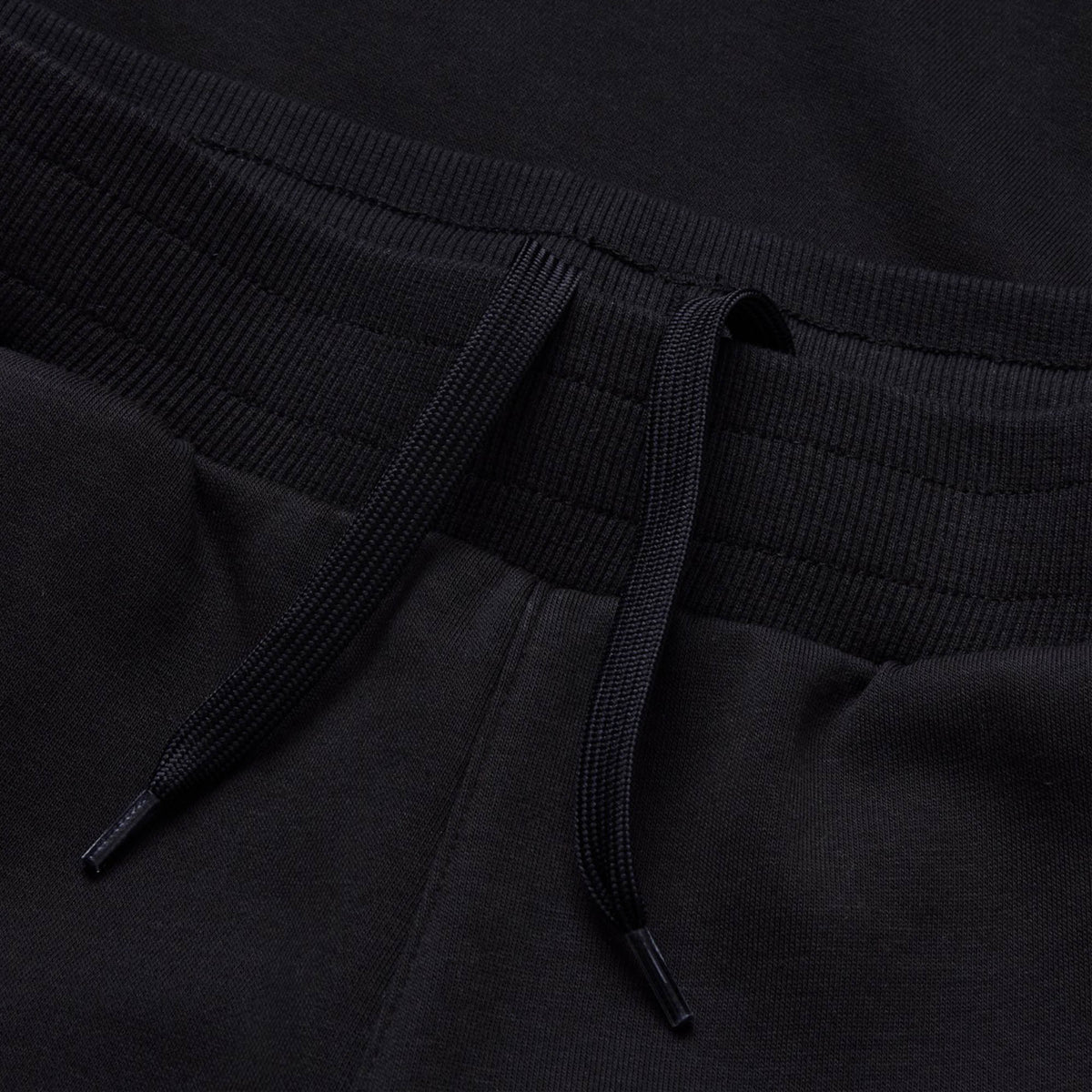 Close-up of the Canterbury Rakaia 2.0 Fleece Pant in black, designed in the classic Canterbury style with an elastic ribbed waistband and loosely tied black drawstrings at the center—perfect as men’s track pants or a comfortable fleece option from Canterbury.