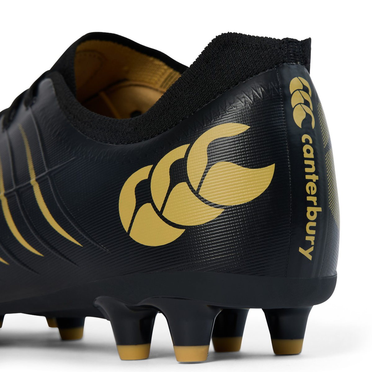 Close-up of the heel of the Canterbury Phoenix 2.0 Pro FG - Black rugby boot, showcasing gold Canterbury logo and branding, with molded studs on the sole designed for lightweight power on firm ground.