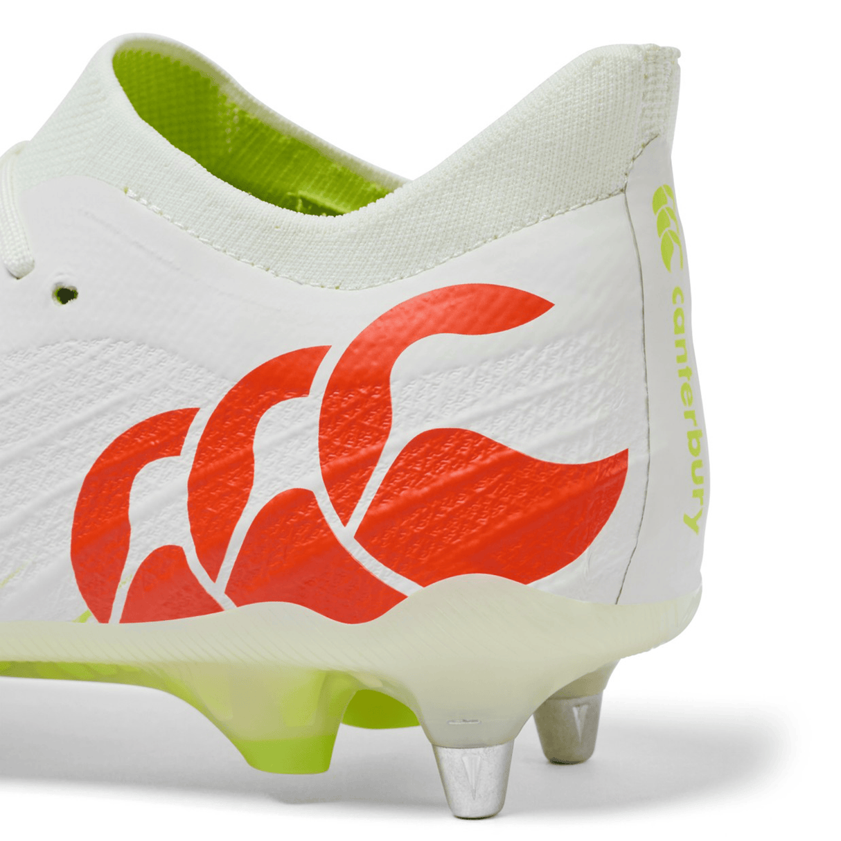Close-up of the heel of the Canterbury Speed Falcon Elite SG - Snow White/Tangerine Tango rugby boot; features red wave logo, yellow "Canterbury" text, metal studs, and light green sole—made for elite performance on soft ground.