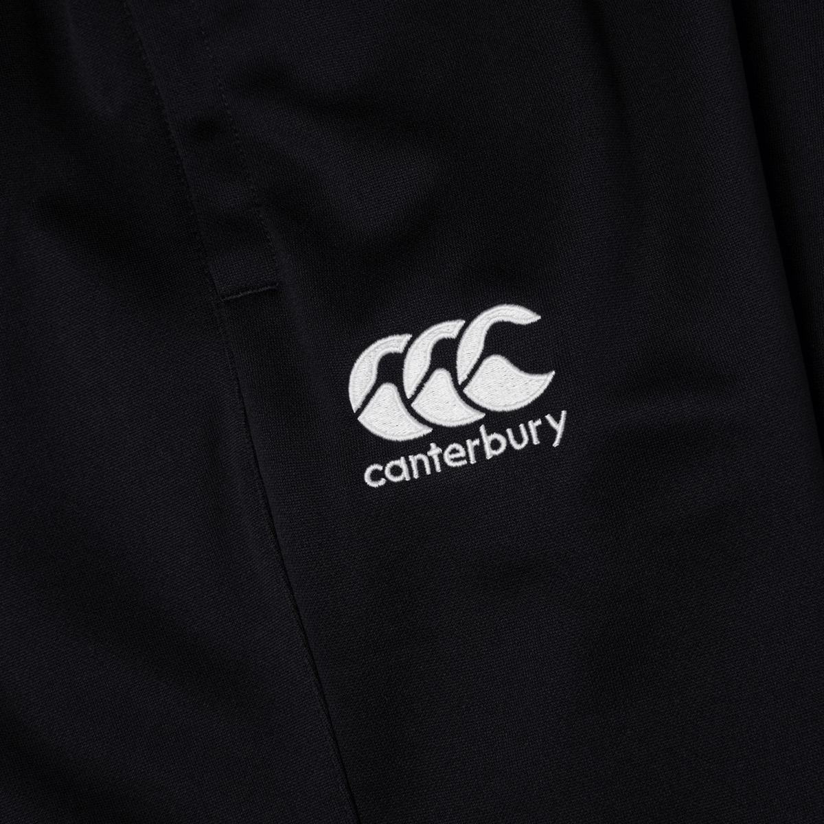 Close-up of black fabric with an embroidered white "Canterbury" logo, perfect for the Canterbury Stretch Tapered Pant by Canterbury.