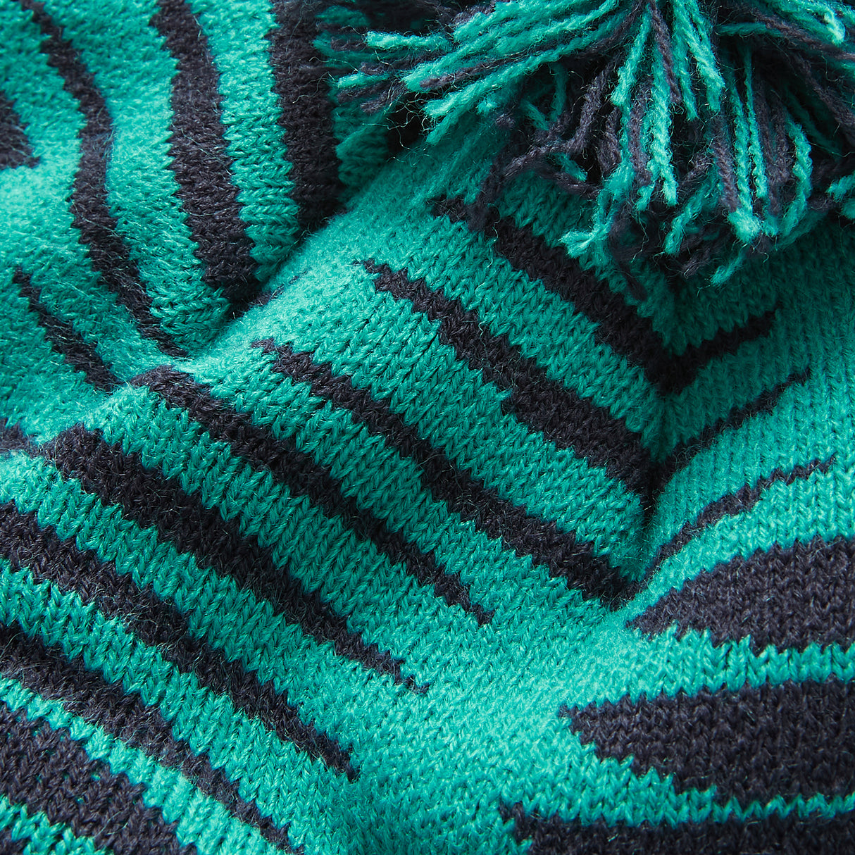 Close-up of a knitted fabric featuring green and black zebra-like stripes and fringed edges, echoing the bold design of the Ireland 26 Bobble Hat by Canterbury.
