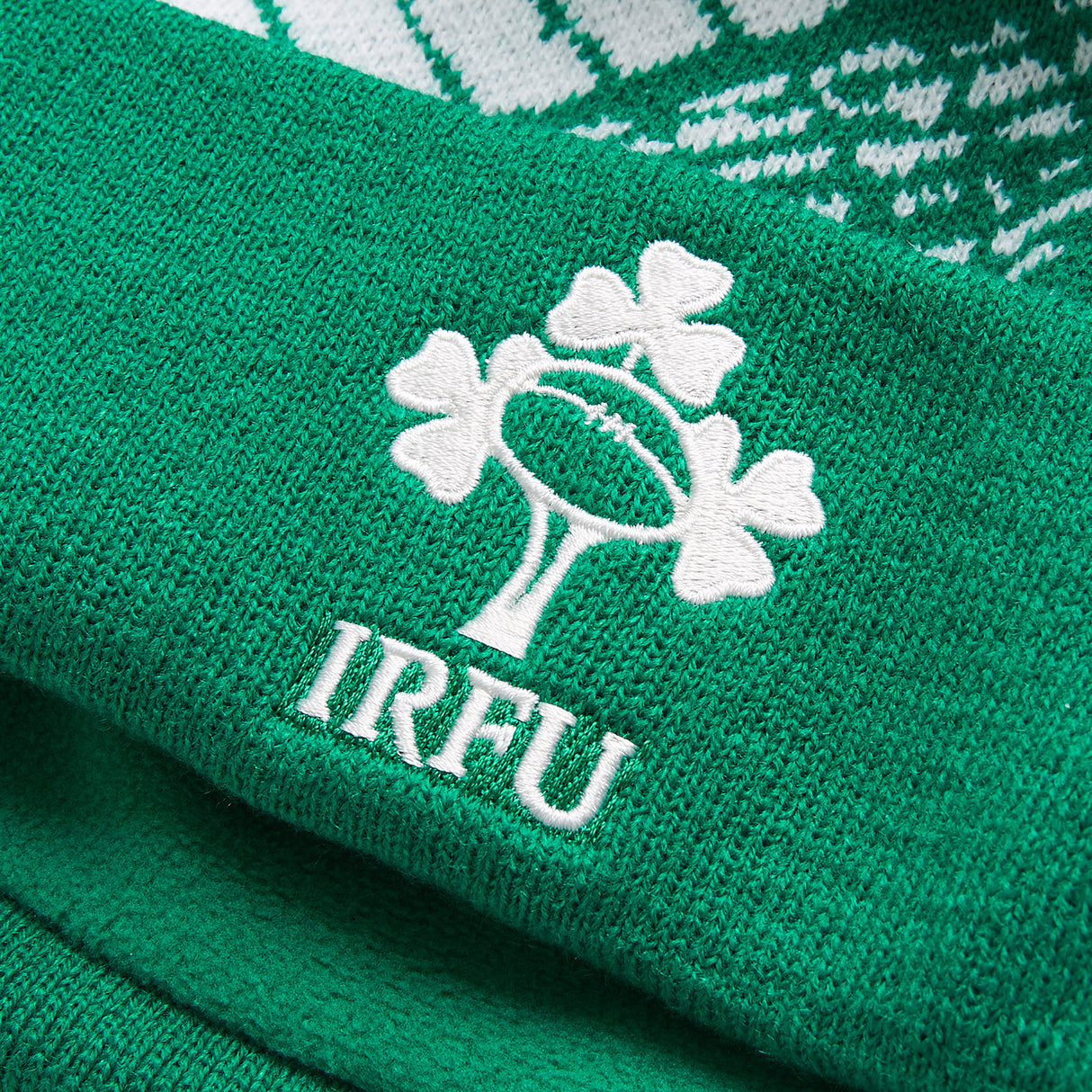 Close-up of a green knit fabric with the IRFU logo—featuring a rugby ball and shamrocks embroidered in white—perfect for an authentic Ireland 26 Bobble Hat by Canterbury.