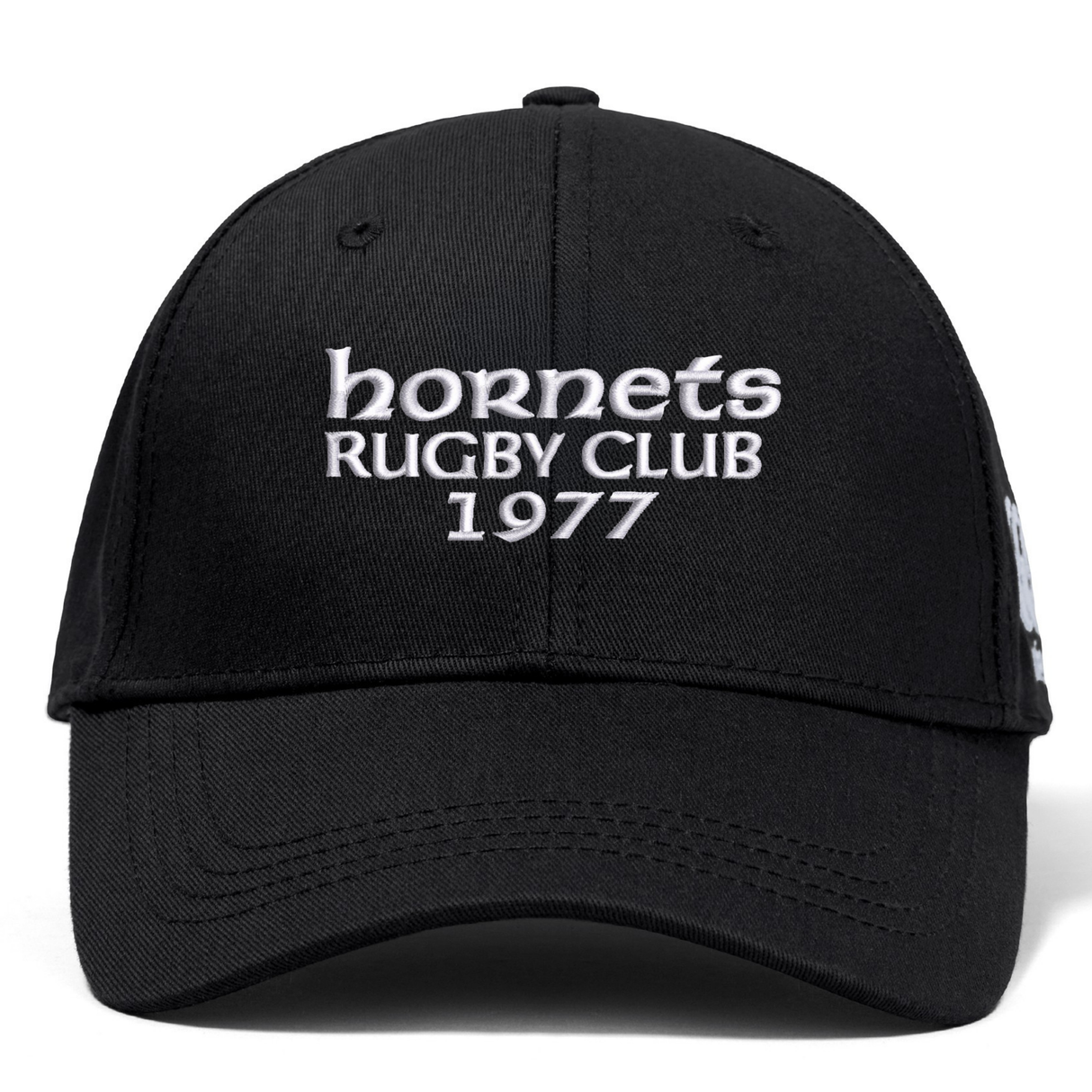 The Hornets Rugby Club 1977 Flexfit Drill Cap by Canterbury features black fabric with white embroidered "hornets RUGBY CLUB 1977" text on the front. This curved brim cap from EMB Canterbury also includes a subtle CCC logo, combining style and comfort for rugby fans.