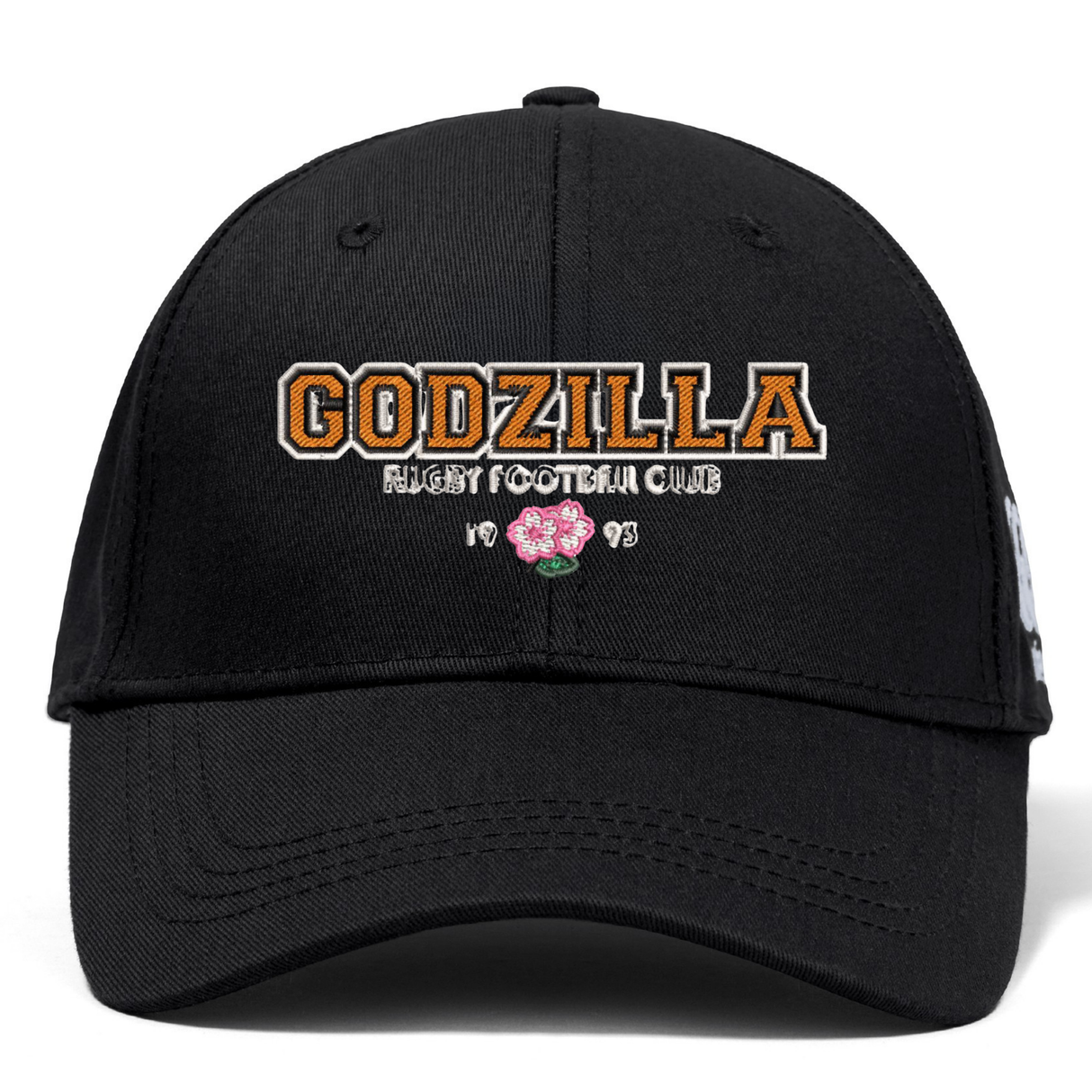 Introducing the Godzilla Rugby Football Club Flexfit Drill Cap by Canterbury from EMB Canterbury—a black cap showcasing “GODZILLA RUGBY FOOTBALL CLUB” embroidered in bold orange and white, accented by a pink flower and “1993” beneath the text on the front. Finished with a curved brim and a sleek CCC logo, this cap delivers an athletic edge to your look.