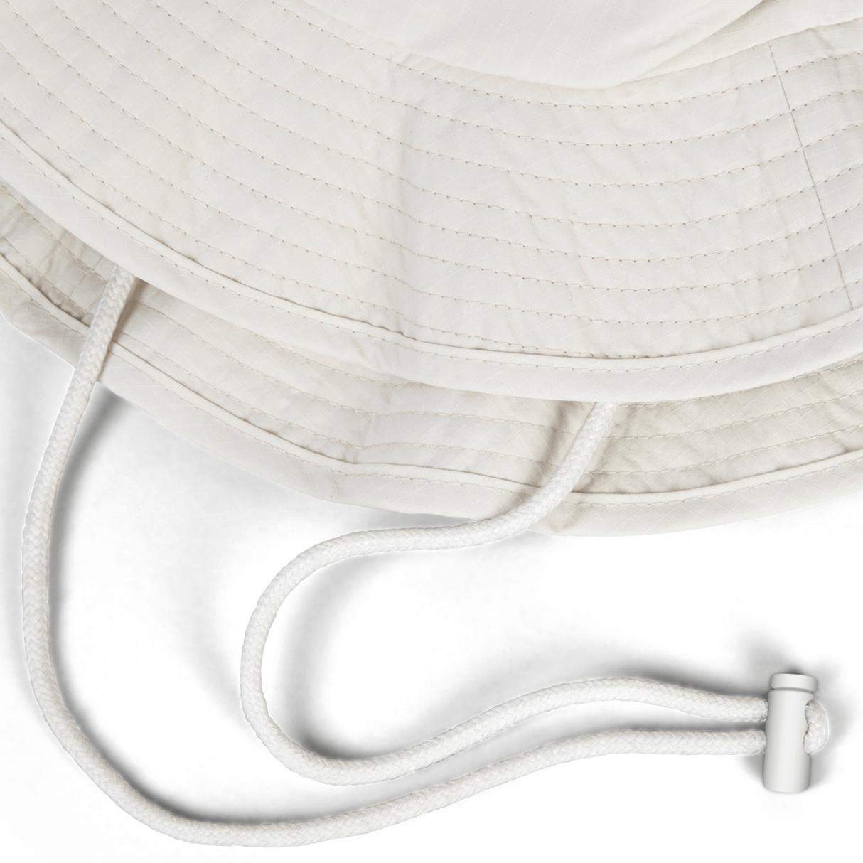 The British & Irish Lions 2025 Outback Wide Brim Bucket Hat by Canterbury is showcased in a close-up, highlighting its beige quilted design. The hat features a white adjustable drawstring with a toggle against a white background and is crafted from quick-dry ripstop fabric for superior comfort and durability.