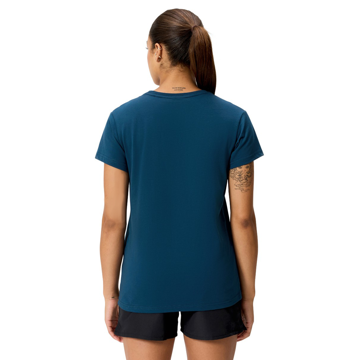 A woman with a ponytail, standing with her back to the camera, wears a blue Women's Uglies Logo T-Shirt by Canterbury and black shorts.