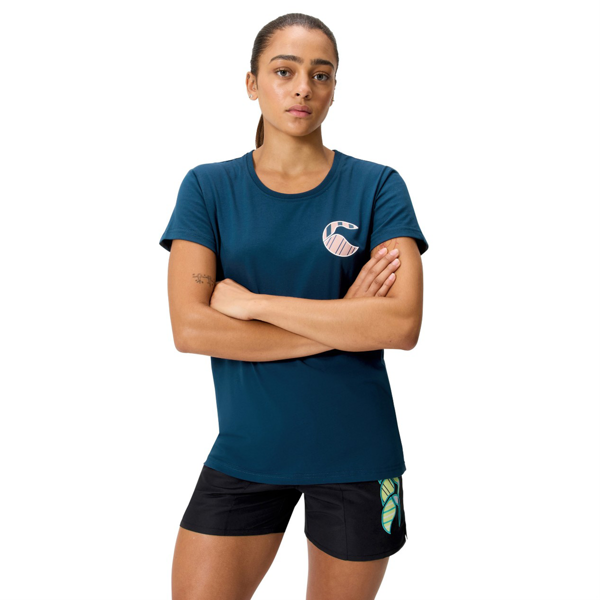 A person stands with arms crossed, wearing the Women's Uglies Logo T-Shirt by Canterbury and black shorts, against a plain white background.