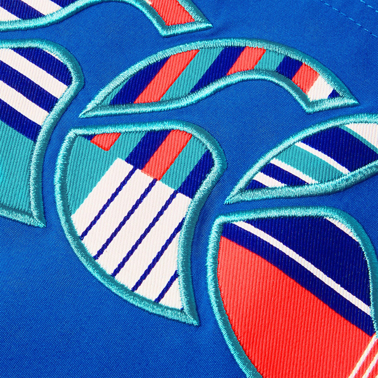 Close-up of Canterbury Uglies Tactic Short by Canterbury, showing blue fabric with colorful embroidered shapes in teal, red, white, and navy blue striped patterns.