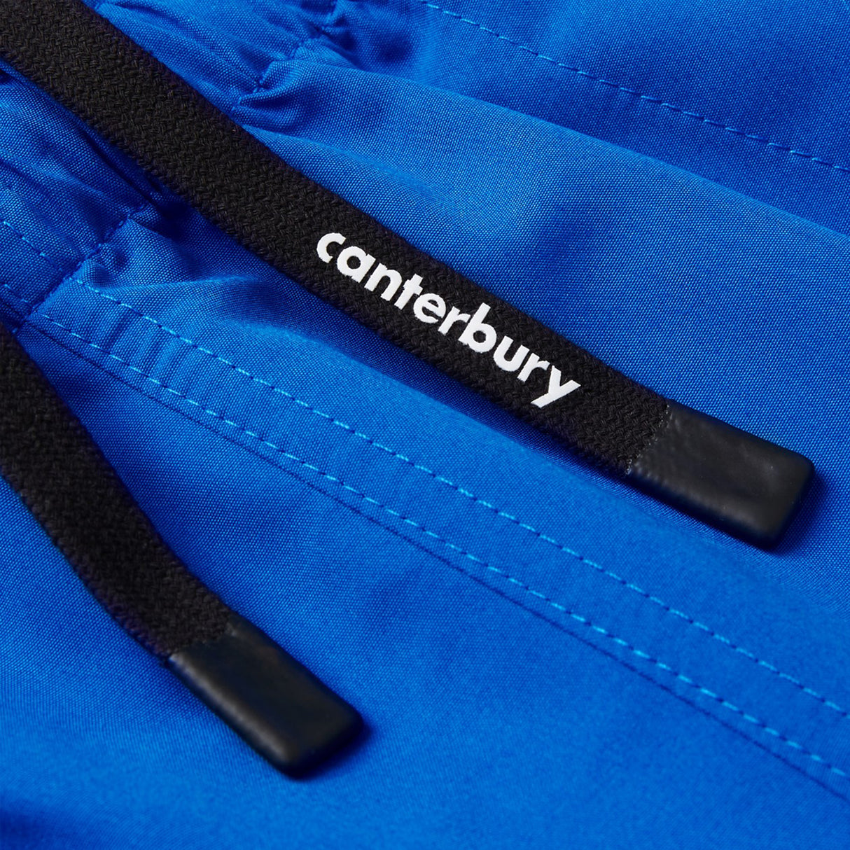 Close-up of black drawstrings featuring "canterbury" in white, attached to bright blue Canterbury Uglies Tactic Short fabric with visible stitching—ideal rugby training shorts from Canterbury.