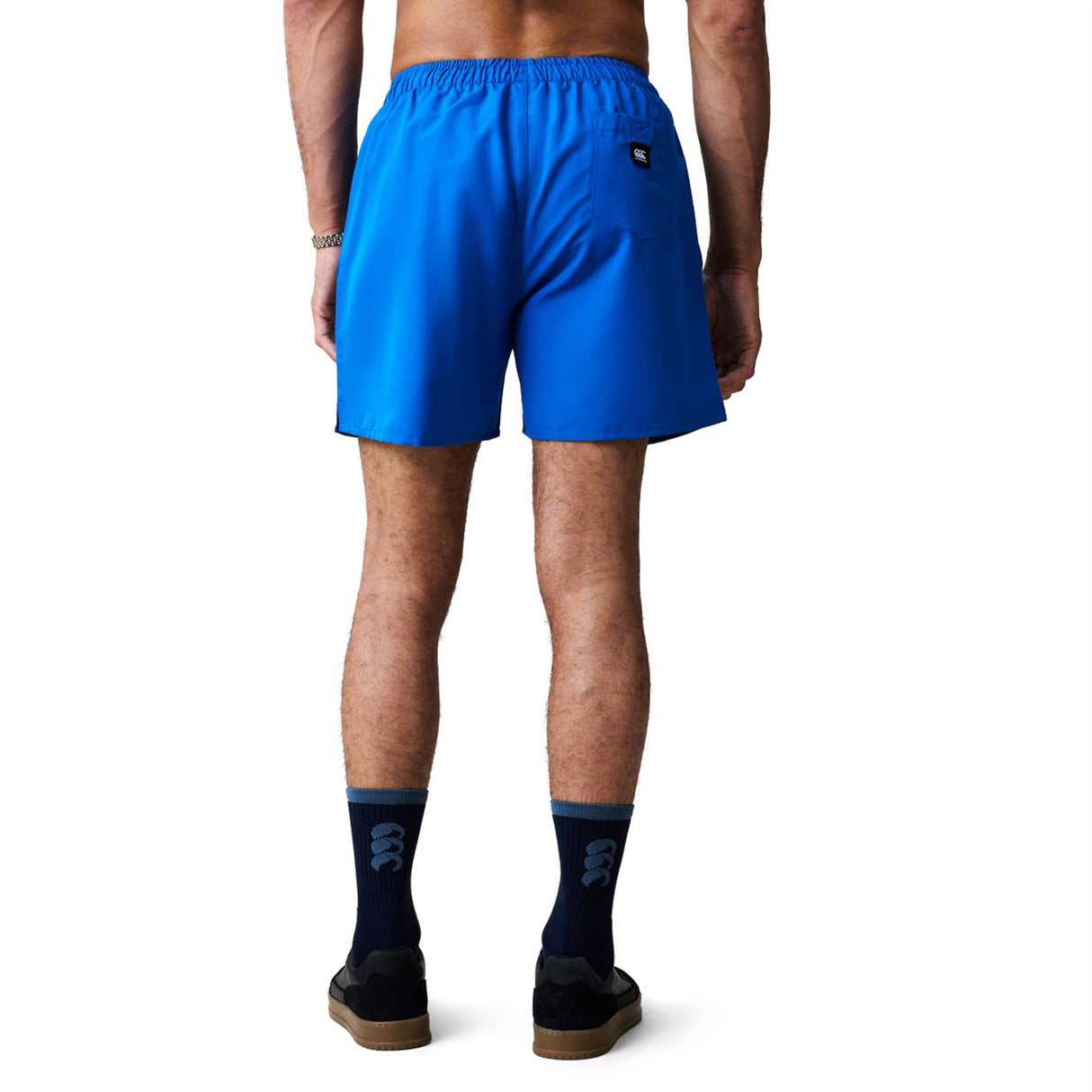 A person stands with their back to the camera, wearing Canterbury Uglies Tactic Short in bright blue, paired with navy socks and black shoes.