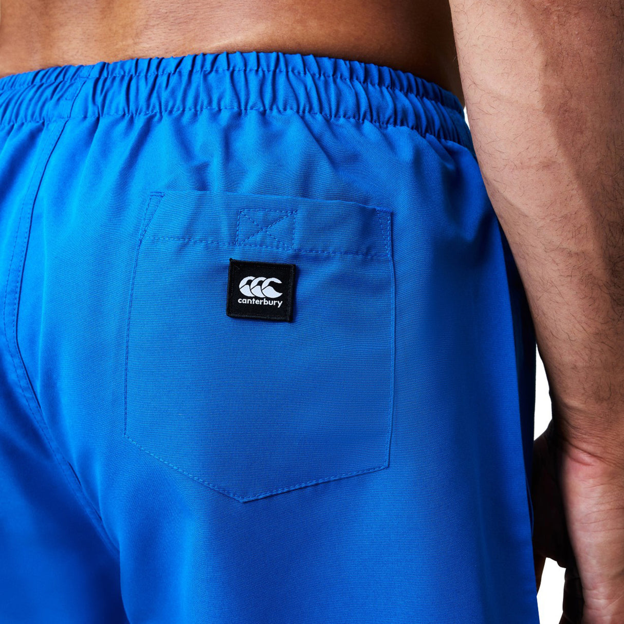Close-up of a person wearing bright blue Canterbury Uglies Tactic Short featuring an elastic waistband and a small black Canterbury logo patch on the back pocket.