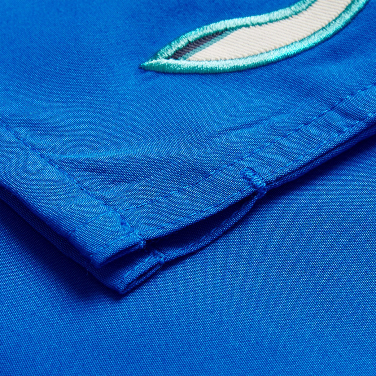 A close-up of Canterbury Uglies Tactic Shorts by Canterbury shows a blue fabric with a folded corner, visible stitching, and part of an embroidered green and white design.