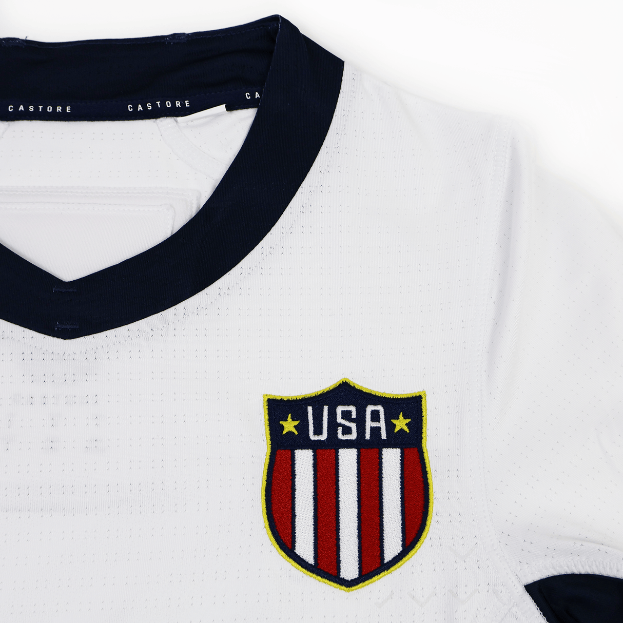 Close-up of the Women's USA Rugby 7s Olympic Pro Away Jersey by Castore in white with a navy collar, featuring a "USA" crest with stars and stripes. "Castore" appears inside the collar—a standout Olympic rugby design.