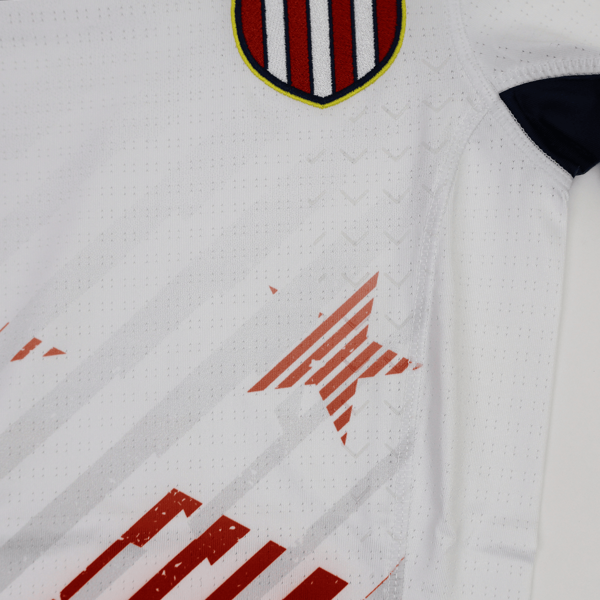 The Women's USA Rugby 7s Olympic Pro Away Jersey by Castore features a white design with a red and blue striped shield on the chest, bold red star accents, and geometric lines—perfect for fans of the USA Rugby 7s team.