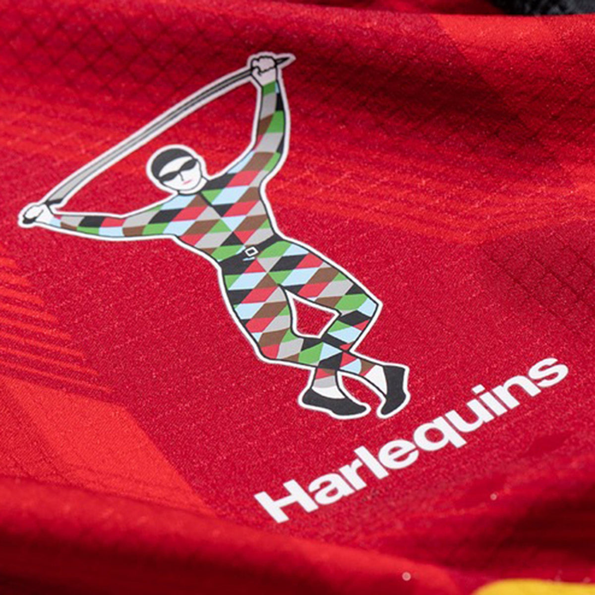 Close-up of the Harlequins 23/24 Pro Home Jersey by Castore, featuring a red design with the Harlequins logo—a stylized jester in a multicolored diamond-patterned suit and "Harlequins" text below.