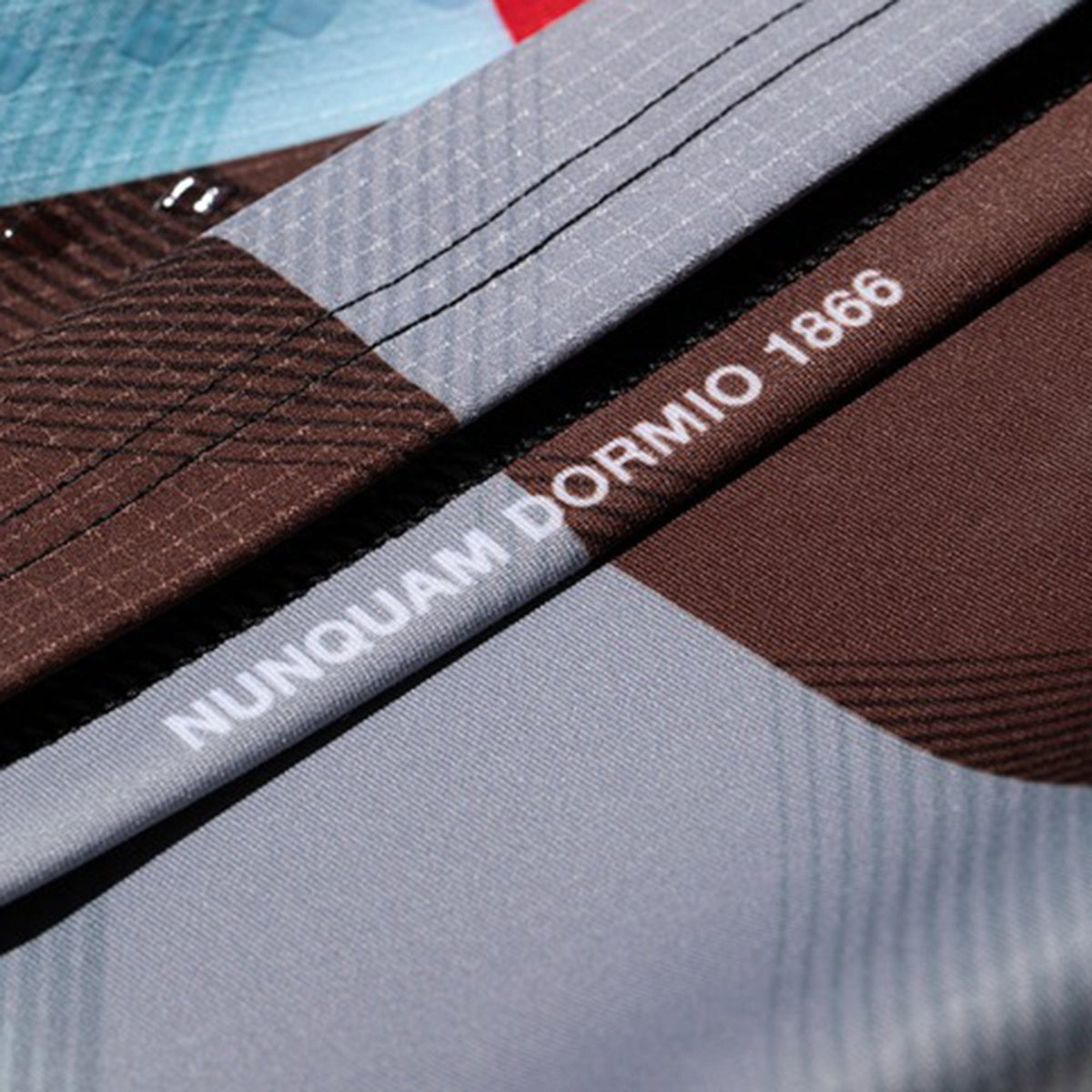 Close-up of fabric with geometric patterns in brown, blue, and gray, plus "NUNQUAM DORMIO 1866" in white—details from the Castore Harlequins 23/24 Pro Home Jersey.