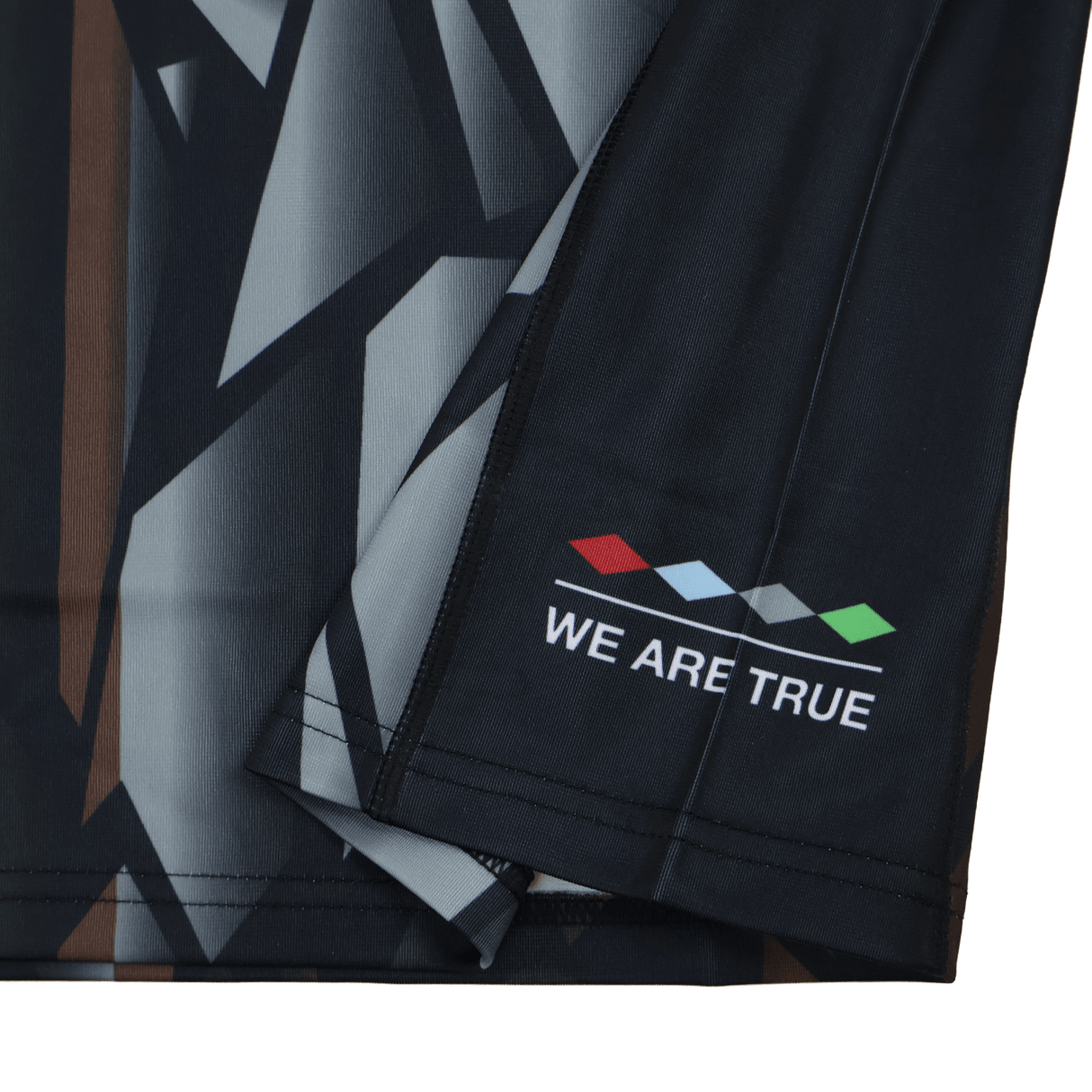 Close-up of the Harlequins 23/24 Replica Third Jersey by Castore, showing a dark geometric fabric with four colored diamonds and "WE ARE TRUE" near the hem—designed as a moisture-wicking football jersey.