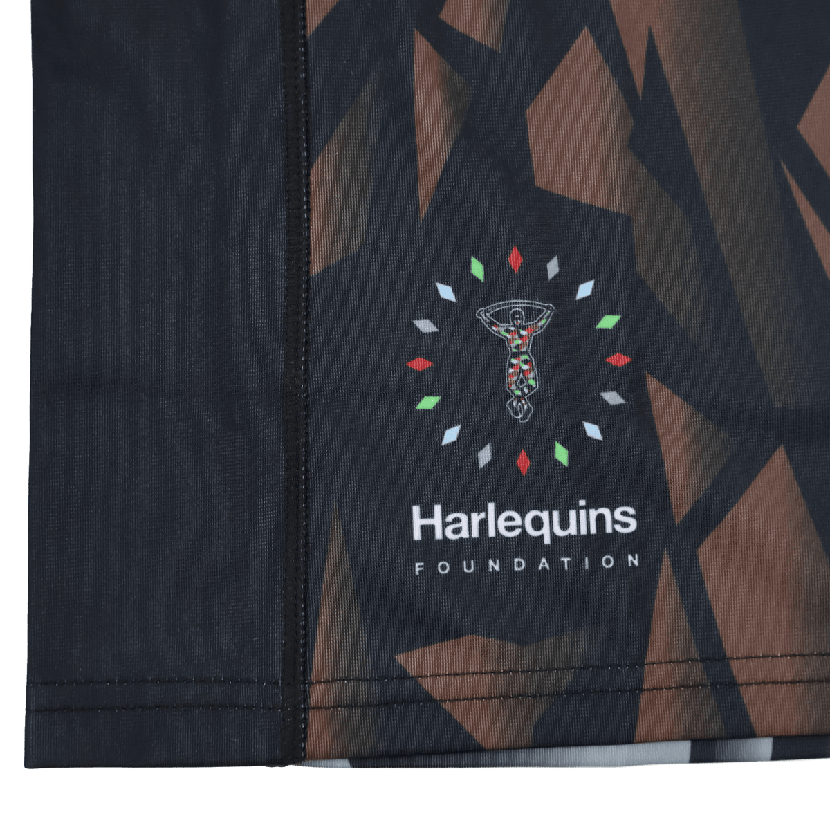 Close-up of the moisture-wicking fabric on the Castore Harlequins 23/24 Replica Third Jersey, showing its abstract geometric pattern and Harlequins Foundation logo with stylized figure amid colored shapes.